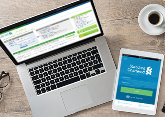 Standard Chartered online banking screen on a laptop and SC Mobile screen on a mobile phone