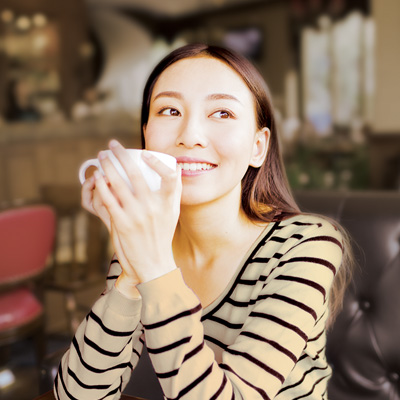 a women holds a coffee cup near her chin, smiles and looks far away
