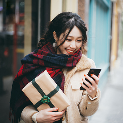 One lady who wearing a scarf holding the gift box and using the mobile device