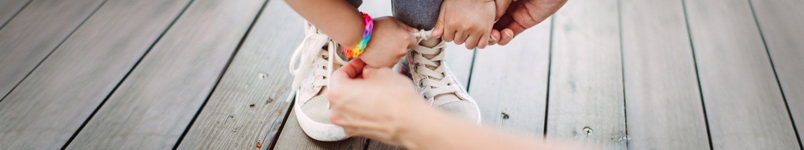 two adult's hands are helping a child fasten the shoelaces