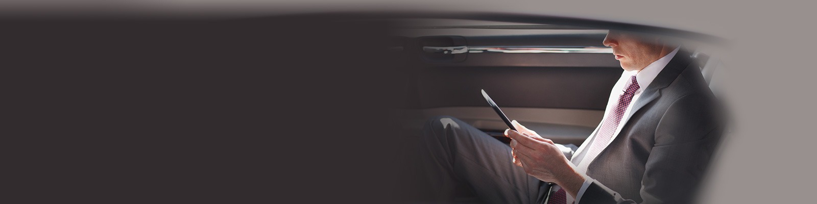 a man sits in a limo, checking on a tablet in his hands
