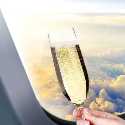 Someone holding a glass of champagne next to the window in an airplane