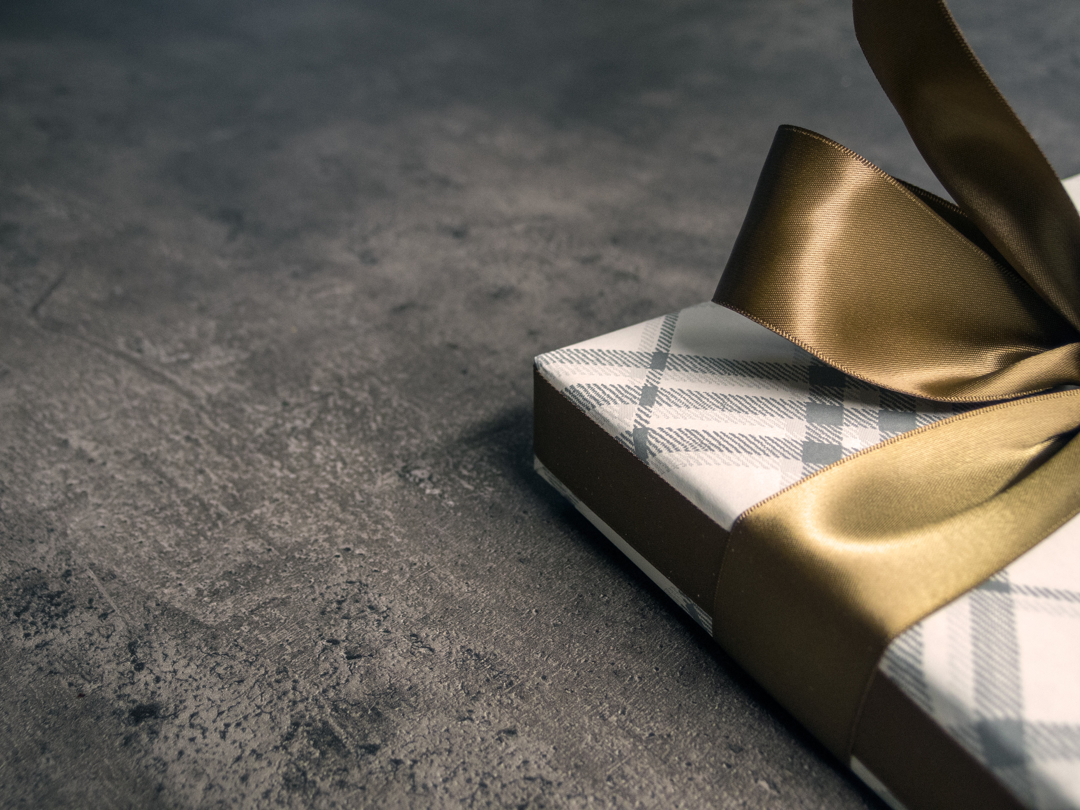 a gift box with checkers wrap and golden ribbon on the concrete floor