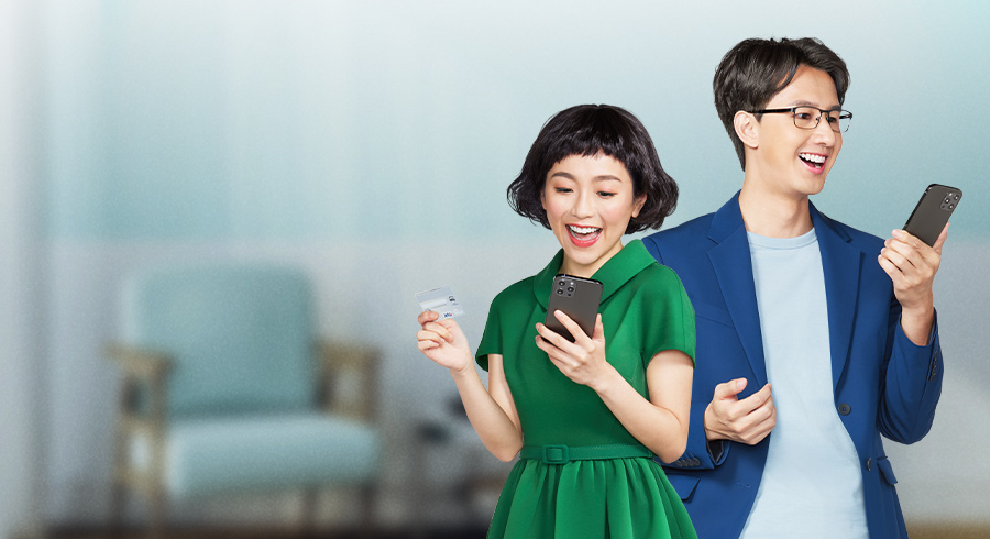 One man who wearing blue suit and one lady who wearing green one piece dress are using their mobile device with smile