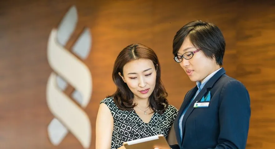 A branch staff talking with a client, background is a Standard Chartered logo
