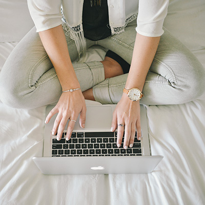 a lady with jeans using her laptop on bed