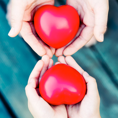 2 pairs of hands holding a red, heart shape decorations