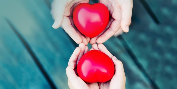 Two hands are carrying red heart decorations