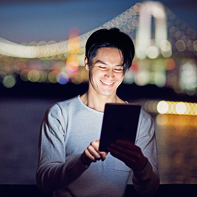 a gentleman watching his tablet with smile, in the night view of cross-harbour bridge