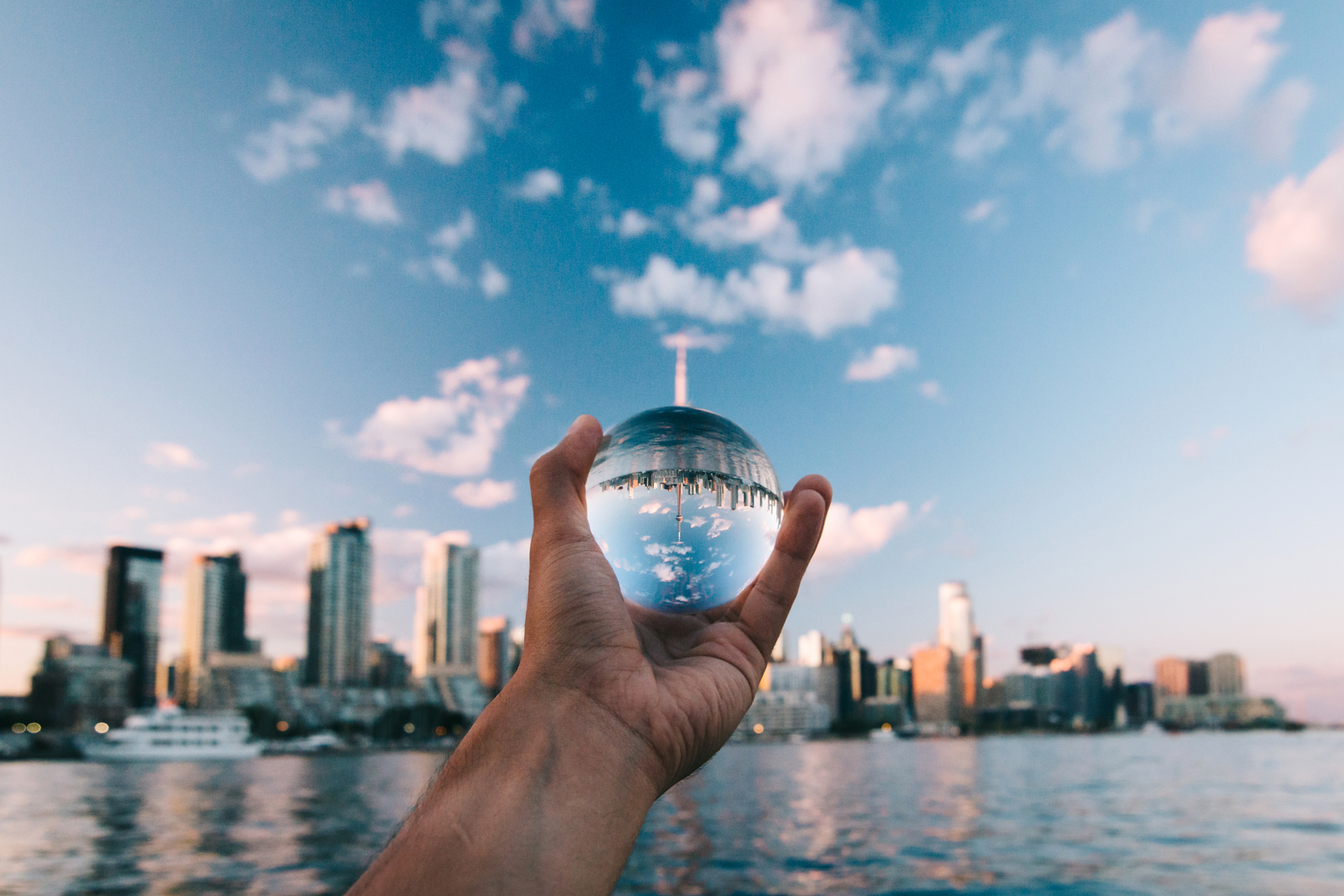 hand holding a crystal ball towards the harbour in daylight, with reflection of the landscape in it