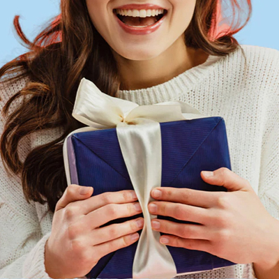 一名穿着白色毛衣的女士高興地抱着藍色的禮品盒