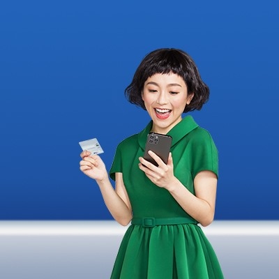 一名身穿綠色連身裙的年輕女士開心地使用她的手機及拿着渣打Smart卡