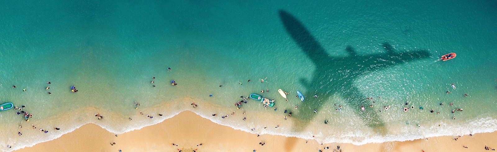 飛機的影子投射在陽光明媚、人多的海灘上
