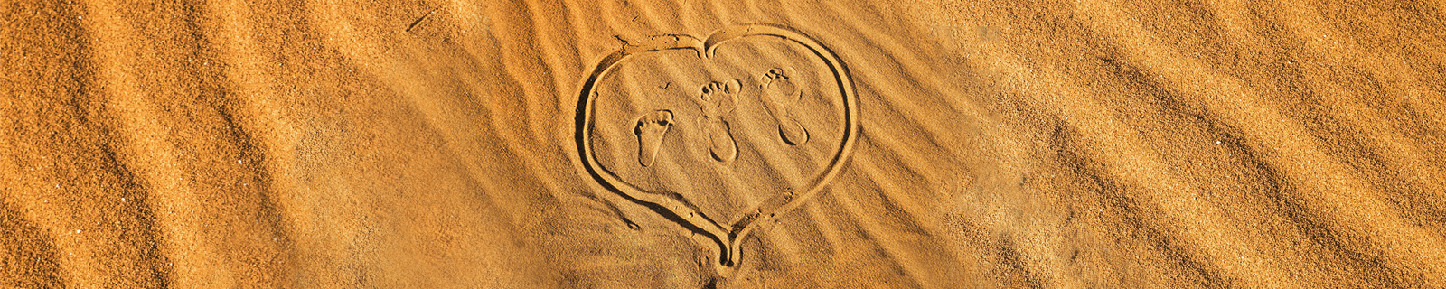 在沙灘上畫出一個心,裡面有兩個大腳印及一個小腳印