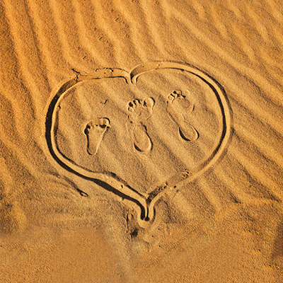 在沙灘上畫出一個心,裡面有兩個大腳印及一個小腳印