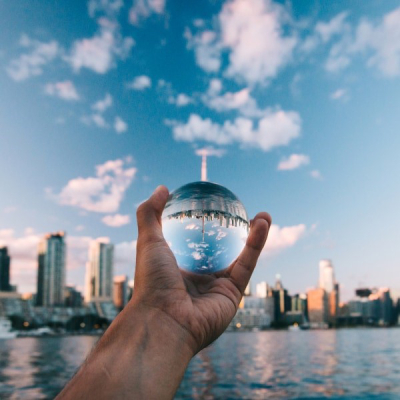 手拿著一個水晶球朝向白天的海港，裡面反射著所有的建築物