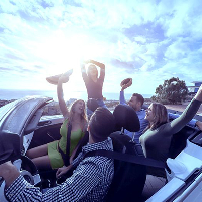 Happy friends with their hands up having fun in cabriolet car on