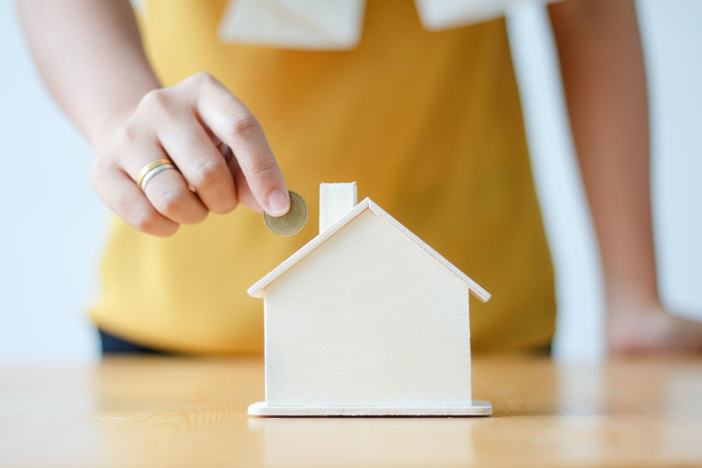 Asian woman putting money coin in to house piggy bank metaphor saving money financial for buy the home shallow depth of field select focus on house