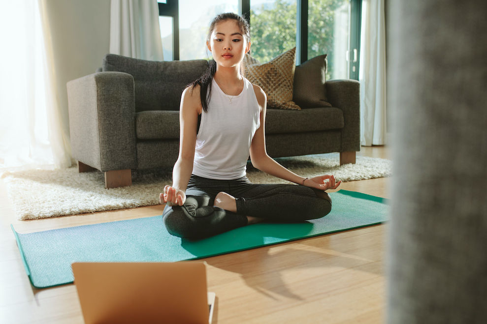 Woman doing yoga while watching instructional videos on laptop