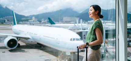 Young asian woman carrying suitcase looking through window at airport terminal while waiting for departure ready for a trip business travel travel and vacation concept