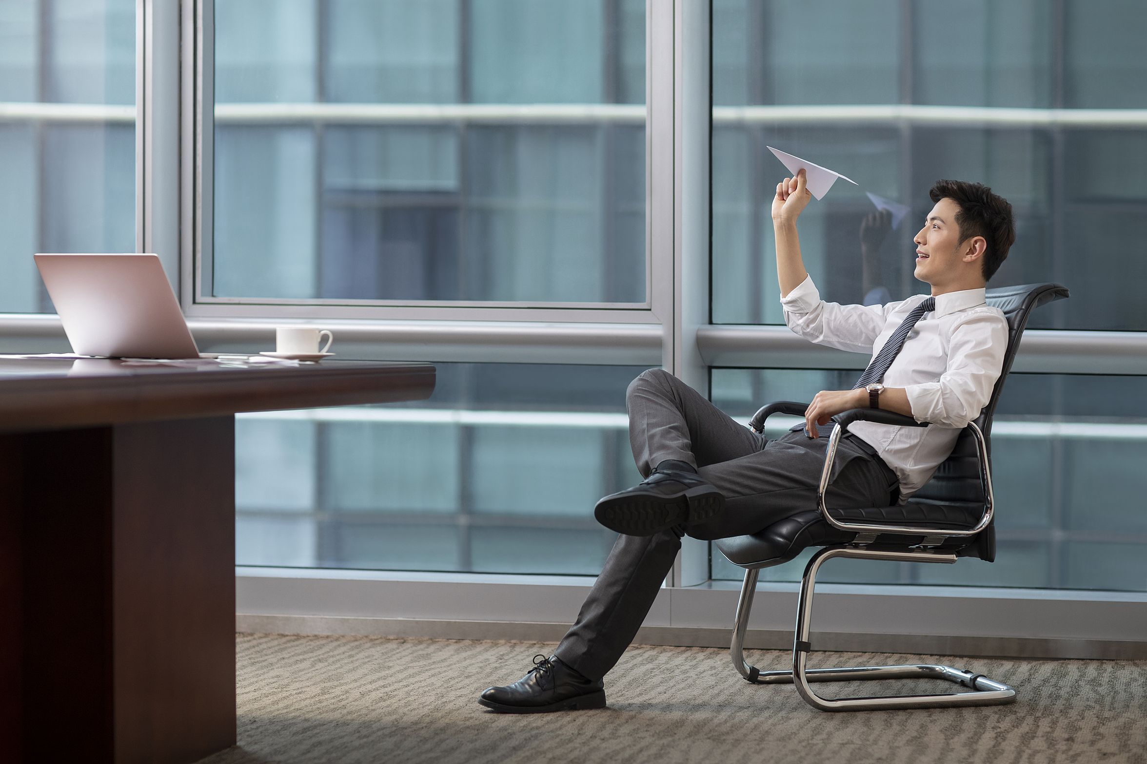 Confident chinese businessman throwing paper plane in office